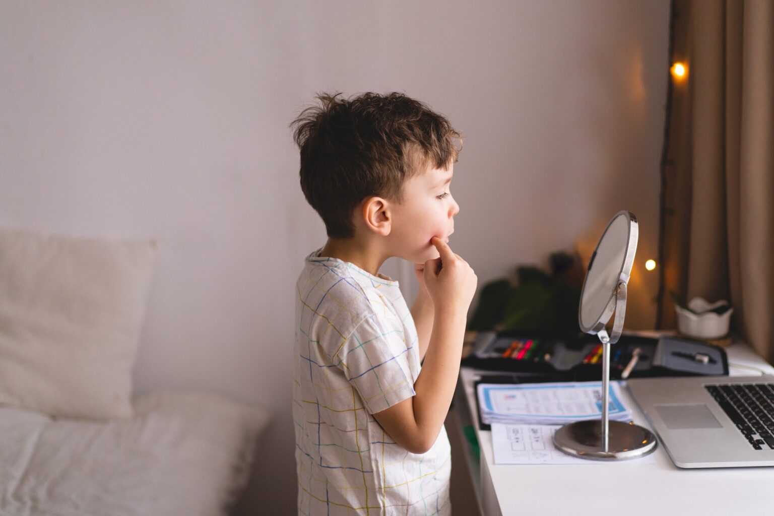 Boy pronouncing sound O looking at mirror doing an online Speech therapy lesson through a laptop